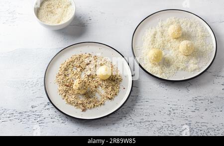 Truffes au chocolat blanc roulé dans des flocons de noix de coco et des noix écrasées sur une assiette blanche. Étape de cuisson de délicieux chocolats Banque D'Images