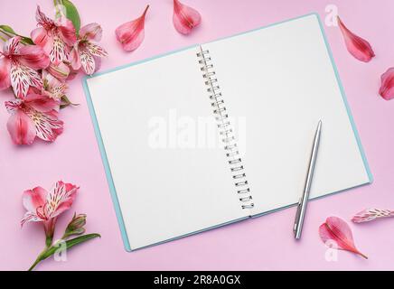 Le carnet est entouré de fleurs et de pétales roses Alstroemeria sur fond rose Banque D'Images
