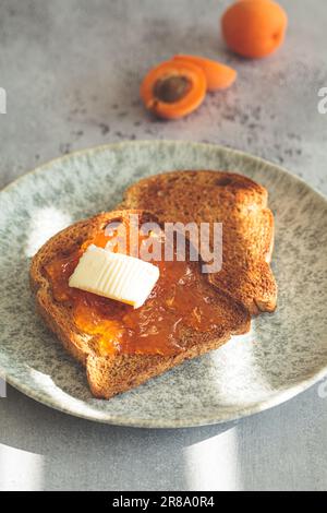 Faire griller avec du beurre et de la confiture d'abricot sur une assiette grise, fond gris. Banque D'Images