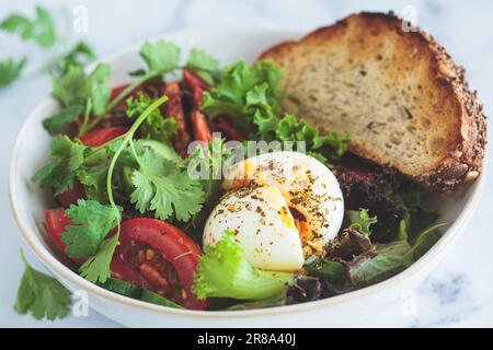 Bol à salade de légumes avec œufs et pain grillé au grain entier pour le petit déjeuner, fond blanc, gros plan. Banque D'Images