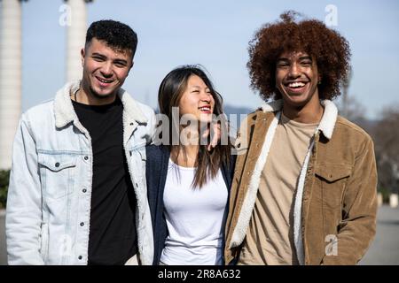 Trois jeunes heureux souriant et ayant l'air détendu dans la rue. Groupe de jeunes enfants du millénaire regardant la caméra rire à l'extérieur. Banque D'Images