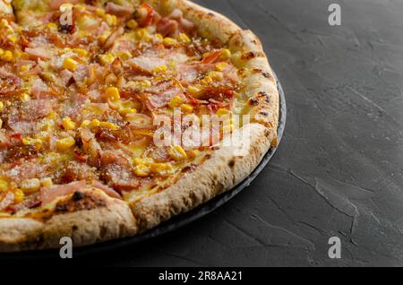 Pizza au jambon et au maïs préparée dans un four à bois. Arrière-plan noir. Parmesan. Banque D'Images