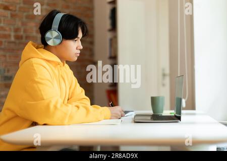 Enfant asiatique faisant le travail à domicile via un ordinateur portable regardant la lecture à l'intérieur Banque D'Images