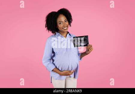 Femme enceinte mauriquement afro-américaine souriante, décontractée et touchante le ventre, émission de sonographie Banque D'Images