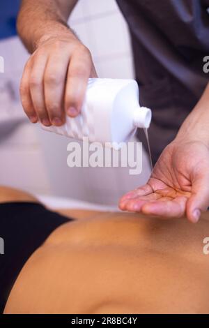 Gros plan des mains du masseur avec de l'huile avant le début de la session dans la clinique ou le salon de beauté. La jeune femme est allongée sur une table de massage en attendant le massage du bac Banque D'Images