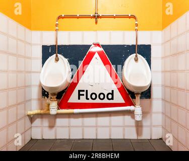 Urinoirs dans une toilette de gents avec un vieux panneau triangulaire d'avertissement de circulation d'inondation Banque D'Images