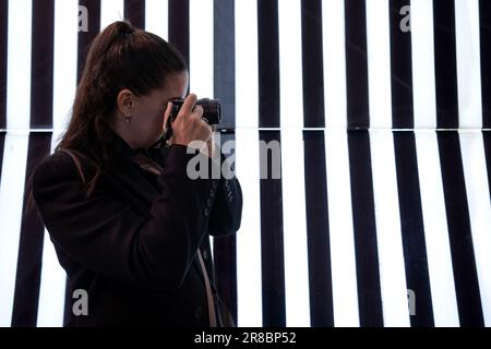 Une jeune femme prenant une photo sur le côté sur un fond lumineux de bandes verticales noires et blanches. Concept de photographie Banque D'Images