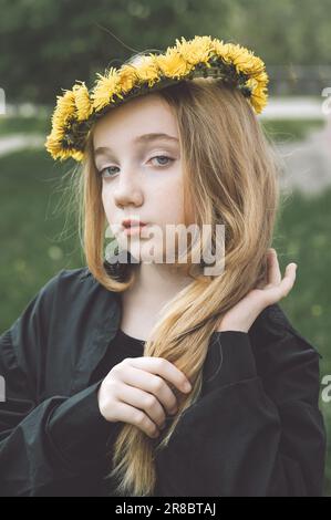 Une fille sérieuse et mystérieuse dans une couronne de pissenlits. tresses une longue tresse de cheveux blonds. Banque D'Images