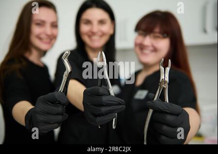 Pinces dentaires en acier inoxydable, pinces pour l'extraction des dents dans les mains gantées d'une équipe floue de dentistes femmes médecins Banque D'Images