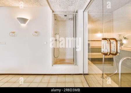 une salle de bains avec une porte de douche en verre et carrelage blanc sur le mur derrière elle est un lavabo, toilettes et miroir Banque D'Images