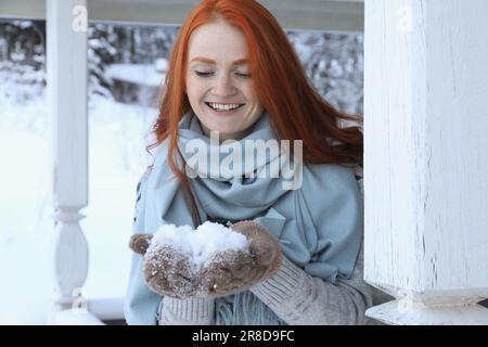 Belle jeune femme tenant de la neige dans un belvédère en bois à l'extérieur. Vacances d'hiver Banque D'Images