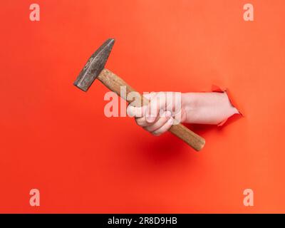 La main d'un homme tient un marteau à travers du papier orange déchiré. Concept, passer à travers le papier orange déchiré. Banque D'Images