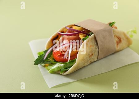 Délicieux emballage de pita avec jamon, frites et légumes sur fond vert clair Banque D'Images