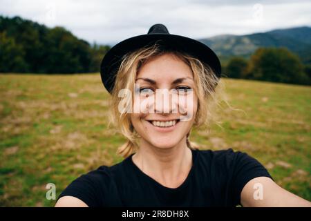 une jeune fille blonde prend un selfie dans un chapeau et un t-shirt noirs. Photo de haute qualité Banque D'Images