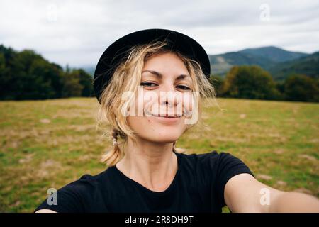 une jeune fille blonde prend un selfie dans un chapeau et un t-shirt noirs. Photo de haute qualité Banque D'Images