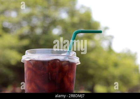 Gros plan de café glacé dans une tasse en plastique. Emporter l'emballage et facile à fraicheur. Vue sur le jardin et arrière-plan bokeh. Banque D'Images