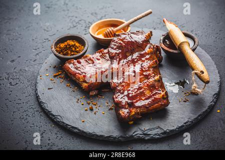 Griller les côtes de porc de rechange avec de la marinade au Chili au miel chaud sur fond noir Banque D'Images
