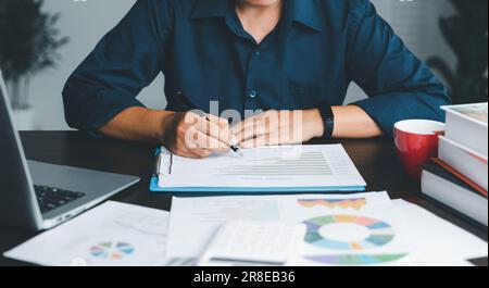 Une jeune femme de garde bancaire utilisant une calculatrice, un ordinateur portable, une feuille de travail papier pour analyser les informations de données. Elle est une financière professionnelle de ba Banque D'Images