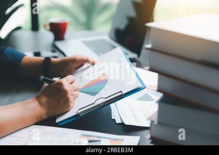 Une jeune femme de garde bancaire utilisant une calculatrice, un ordinateur portable, une feuille de travail papier pour analyser les informations de données. Elle est une financière professionnelle de ba Banque D'Images