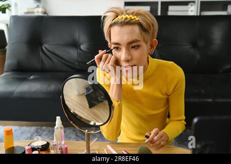 Joyeux jeune gay homme blogger enregistrement maquillage tutorial, streaming en direct à la maison. LGBTQ Lifestyle, influenceur, blogueur Banque D'Images