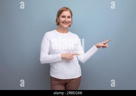 bonne santé blonde moyenne femme dans un chandail blanc dans la phase préménopausique pointe son doigt sur le côté Banque D'Images