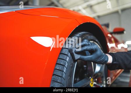 Gros plan de pneus noircissants voiture de détail d'une voiture de sport rouge. Processus d'habillage des voitures. Nettoyage des pneus avec une éponge. Photo de haute qualité Banque D'Images