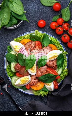 Salade Périgord avec foie de poulet rôti, tomates rouges, concombres, œufs durs, laitue et épinards. Arrière-plan de la table de cuisine noire, vue du dessus Banque D'Images