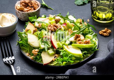 Salade Waldorf aux pommes rouges et vertes, céleri cru, laitue, arugula et noix avec sauce mayonnaise, fond de table noir, vue du dessus Banque D'Images