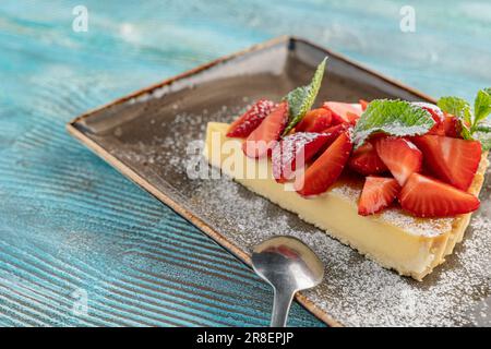 Tranche de cheesecake avec fraises. Cheesecake New-yorkais de style classique sur fond bleu en bois Banque D'Images