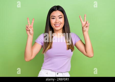 Photo portrait de jolie fille chinoise vietnamienne montrer double V-signe habillé élégant violet ensemble isolé sur fond vert couleur Banque D'Images