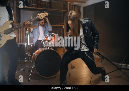 Un rocker expressif chantant dans le microphone pendant que son groupe joue du métal lourd Banque D'Images