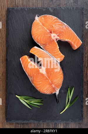 Steaks de saumon et branches de romarin crus sur une planche à servir en mica sur fond de bois. Copier l'espace. Banque D'Images