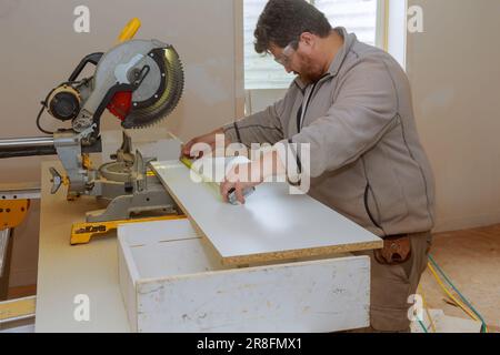 Un employé utilise une scie circulaire pour couper le carton de mélamine pour les étagères à l'aide d'une scie Banque D'Images