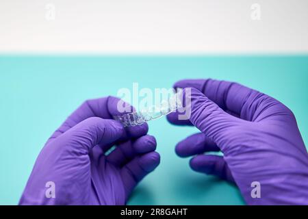 Technicien dentaire avec un corset invisible dans un laboratoire dentaire, portant des gants violets et une table verte. Banque D'Images