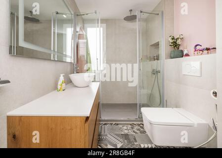 Salle de bains avec lavabo en résine blanche sur mobilier en bois et miroir avec connexion USB et cabine de douche avec écrans transparents Banque D'Images