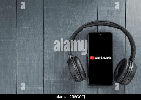 Pologne, Varsovie - 21 juin 2023 : application YouTube Music phone. Lecteur vidéo sur l'écran du téléphone portable et casque sans fil sur fond sombre Banque D'Images