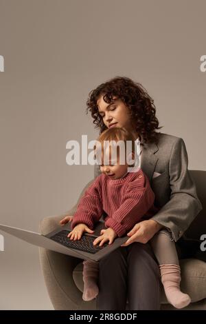 construire une carrière réussie, équilibre de vie professionnelle, parent de travail, femme d'affaires maussette utilisant un ordinateur portable et assis sur un fauteuil avec fille, mère et chil Banque D'Images