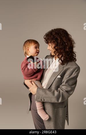 parent moderne, construire une carrière réussie, l'équilibre entre le travail et la vie, mère gaie tenant dans les bras fille de tout-petit avec smartphone sur gre Banque D'Images