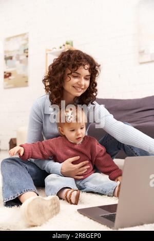 un parent moderne qui travaille, qui s'engage avec son enfant, qui équilibre entre travail et vie, une femme heureuse qui utilise son ordinateur portable dans un salon confortable, un parent moderne, un woma multitâche Banque D'Images