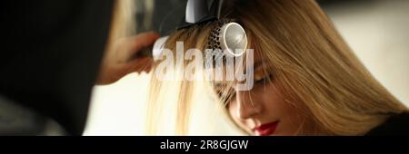 Séchage des cheveux blonds avec sèche-cheveux et brosse ronde dans le salon de coiffure Banque D'Images