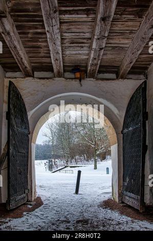 Une scène hivernale blanche avec une porte en bois ornée menant à un parc enneigé, avec une couverture de neige blanche couvrant le sol Banque D'Images
