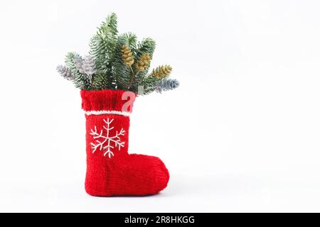 Chaussette de Noël rouge avec un flocon de neige blanc brodé et des branches vertes d'un sapin de Noël sur fond gris avec un emplacement pour le texte. Banque D'Images