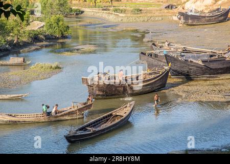 Plusieurs petits bateaux traditionnels en bois sont amarrés dans un plan d'eau calme avec des personnes à proximité Banque D'Images