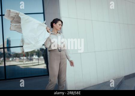 Portrait d'une belle jeune femme d'affaires réussie en costume de pantalon beige debout contre le quartier de bureau, espace de copie Banque D'Images