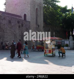 Vendeur assis à côté d'un chariot rouge vendant Simits aka bagels turcs par l'entrée de style forteresse construite en pierre Gulhane Park à Istanbul en Turquie Banque D'Images