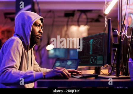 Hacker dans le capot violant l'entreprise système de cybersécurité sur l'ordinateur. Un jeune homme afro-américain enfreint la loi tout en craquant le mot de passe et en utilisant des logiciels malveillants de virus d'Internet Banque D'Images