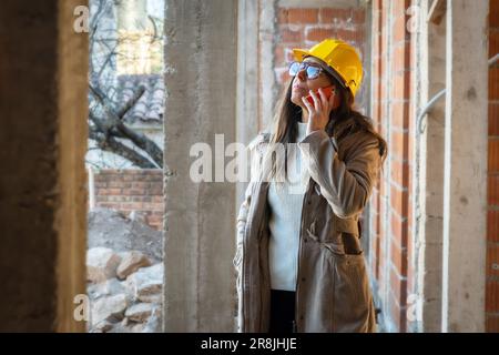 Portrait d'une femme bâtisseuse réussie avec un casque de sécurité jaune, faisant un appel avec son téléphone cellulaire. Portrait d'une femme architecte debout regardant c Banque D'Images