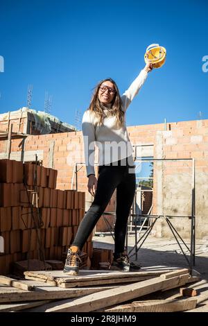 Femme ingénieure mature. Portrait vertical d'une femme architecte debout souriant et regardant l'appareil photo avec son chapeau rigide jaune le tenant Banque D'Images