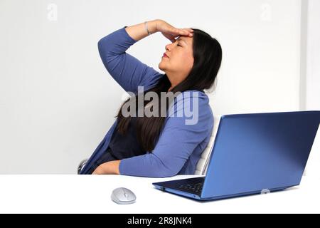 Latina, âgée de 40 ans, souffre de douleurs au dos, au cou et à la tête dues au stress et à l'épuisement professionnel lorsqu'elle travaille au bureau avec son ordinateur portable Banque D'Images