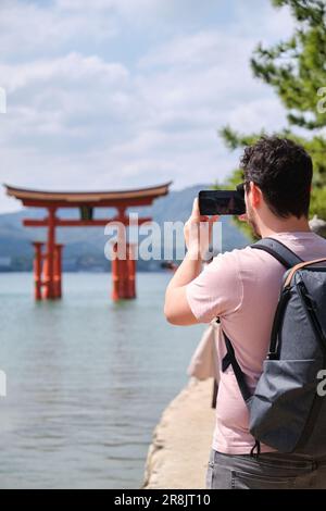 Touriste européen prenant des photos d'Itsukushima Jinja Otorii ou de la porte du Grand Torii sur la mer de Miyajima, Hiroshima, Japon. Banque D'Images